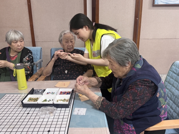 一暄康养华阳院长者在志愿者帮助下编制五彩绳